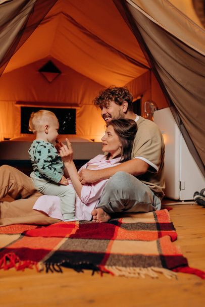 Glückliche Familie mit schönen Baby spielen und verbringen Zeit zusammen im Glamping am Sommerabend. Luxus-Zeltlager für Erholung und Erholung im Freien. Lifestyle-Konzept - Foto, Bild