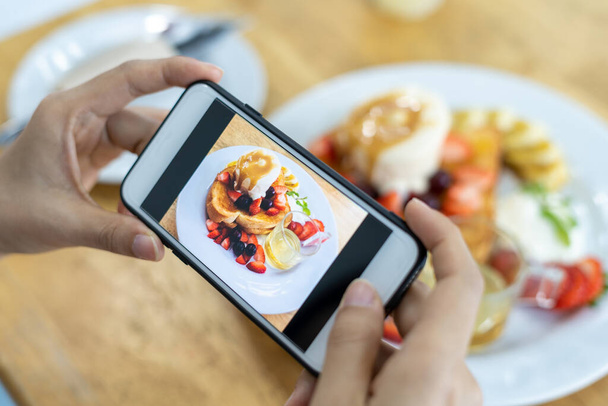 владелец ресторана фотографирует еду на столе со смартфоном для размещения на сайте. Онлайн доставка еды, услуга заказа, влиятель, обзор, социальные сети, доля, маркетинг, интерес - Фото, изображение