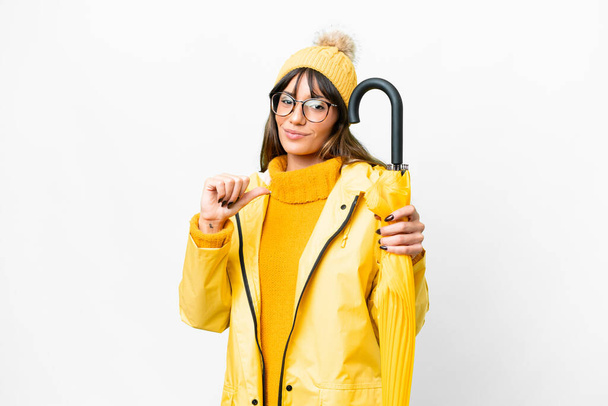 Young caucasian woman with rainproof coat and umbrella over isolated white background proud and self-satisfied - Φωτογραφία, εικόνα