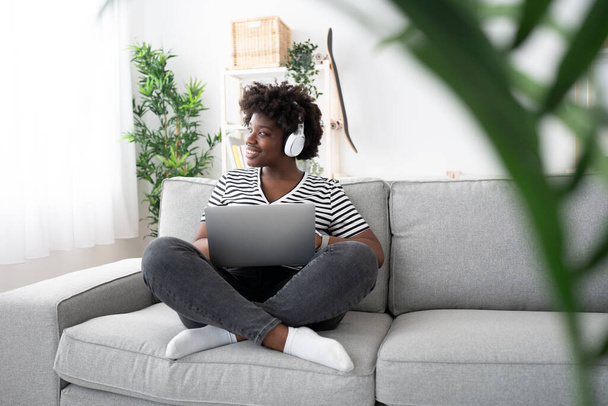 afro-américaine travail de la maison sur ordinateur portable tout en étant assis sur canapé. - Photo, image