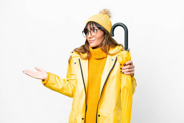 Young caucasian woman with rainproof coat and umbrella over isolated white background with surprise expression while looking side - Foto, imagen
