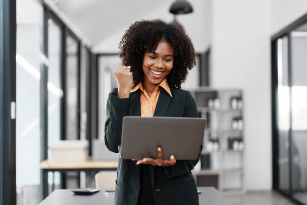 Belle jeune adolescente américaine africaine femmes d'affaires tenant ordinateur portable avec les mains en l'air dans le gagnant est geste, heureux d'être réussi à célébrer la réussite. - Photo, image