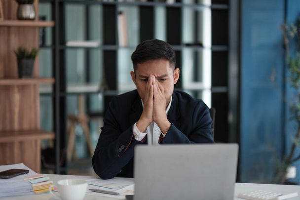 A businessman looks tiredly at a computer monitor and feels hopeless. A young man in a suit works in the office... - Photo, image