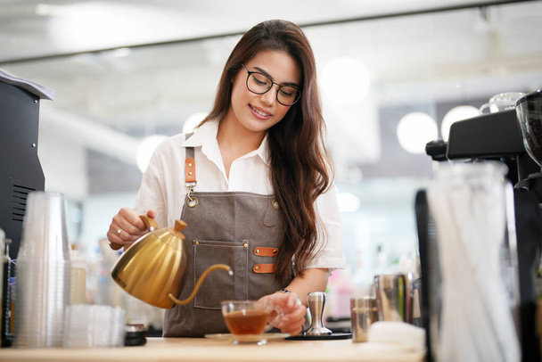 Portret van een gelukkige vrouw in haar winkel. Vrolijke serveerster wacht op klanten in de coffeeshop. Succesvolle kleine ondernemer in casual dragen van grijze schort - Foto, afbeelding