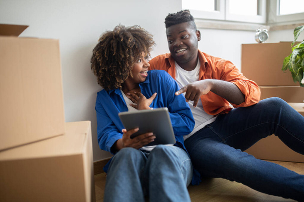 Iloinen musta pari, jolla on hauskaa digitaalisen tabletin kanssa valitessaan huonekaluja uuteen kotiinsa, onnelliset nuoret afroamerikkalaiset puolisot käyttävät nykyaikaista gadgetia verkkokauppaan muuttaessaan taloa. - Valokuva, kuva
