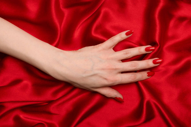 Gyönyörű piros manikűr női kéz egy luxus piros selyem háttér.  - Fotó, kép