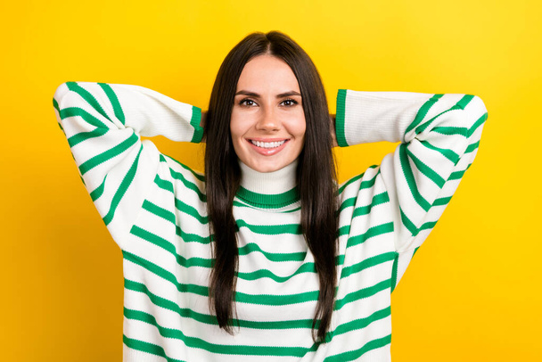 Photo of pretty shiny lady dressed striped pullover arms behind head smiling isolated yellow color background. - 写真・画像