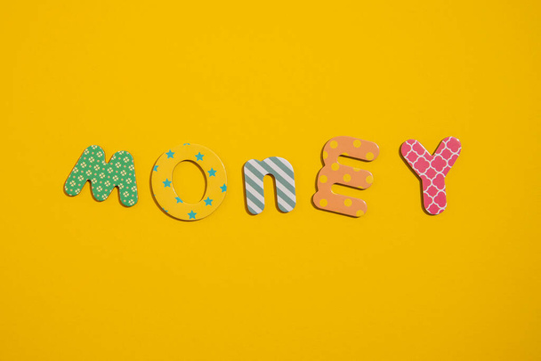The word money from multi-colored letters of the alphabet on a yellow background. Top view, flat lay. - Photo, Image