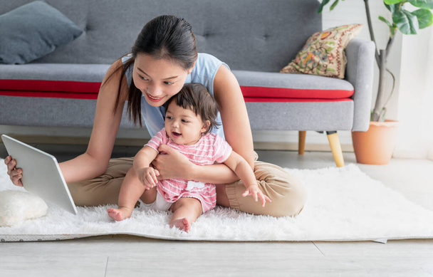 Asian mother and 7 month old daughter sitting on the floor and looking at a tablet, to relationship in family and infant education concept. - Foto, imagen
