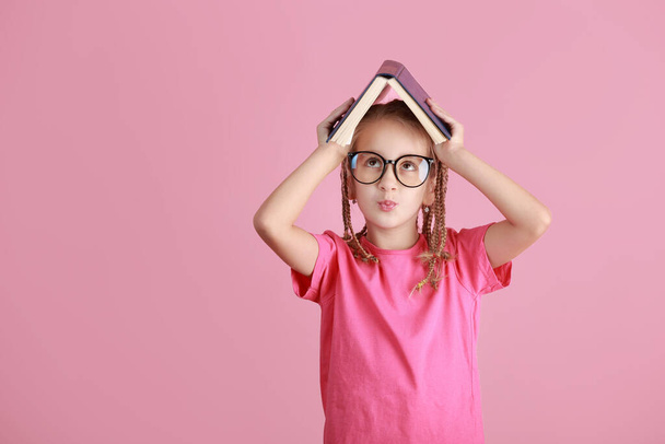Vissza a tantervhez. Mosolygó, csinos, szemüveges iskolás lány úgy tartja a könyvet a feje fölött, mint egy rózsaszín háttéren elszigetelt tetőt. Gyerekkori életmód koncepció. Iskolai oktatás. Szeptember 1.. - Fotó, kép