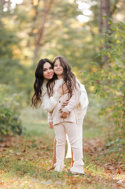 Mothers day. Beautiful smiling young mom with teen daughter are hugging and looking at camera outdoors in the autumn park. Family day. Idyllic stylish family of two communicate alone. happy childhood - Fotografie, Obrázek