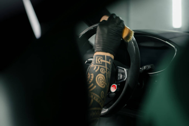 Worker cleans steering wheel professional brush and clout microfiber Professional car wash and detailing Interior detailing - 写真・画像