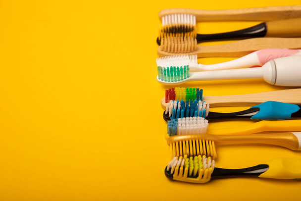 Electric and manual toothbrushes on a yellow background. View from above. Oral hygiene. Ordinary toothbrush, eco and electric toothbrush. Oral hygiene. Oral Care Kit. Dentist concept. Dental care. - Fotoğraf, Görsel