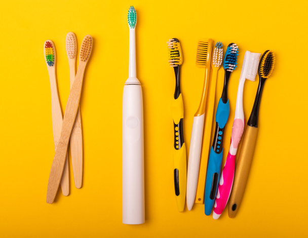 Electric and manual toothbrushes on a yellow background. View from above. Oral hygiene. Ordinary toothbrush, eco and electric toothbrush. Oral hygiene. Oral Care Kit. Dentist concept. Dental care. - Photo, Image