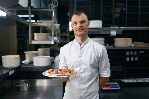 Portret van een mannelijke pizzaiolo met vers gekookte pizza. Koken school master class of Italiaanse fast food restaurant presentatie - Foto, afbeelding