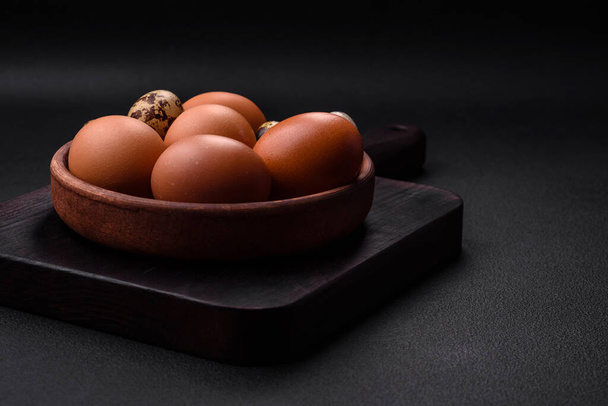 Rohe Hühner- und Wachteleier in einer braunen Keramikschale auf dunklem Betongrund. Ostervorbereitungen - Foto, Bild