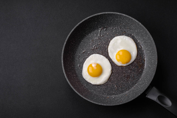 揚げ卵とおいしい栄養価の高い英語の朝食,トマト,ダークコンクリートの背景にベーコンと豆. - 写真・画像