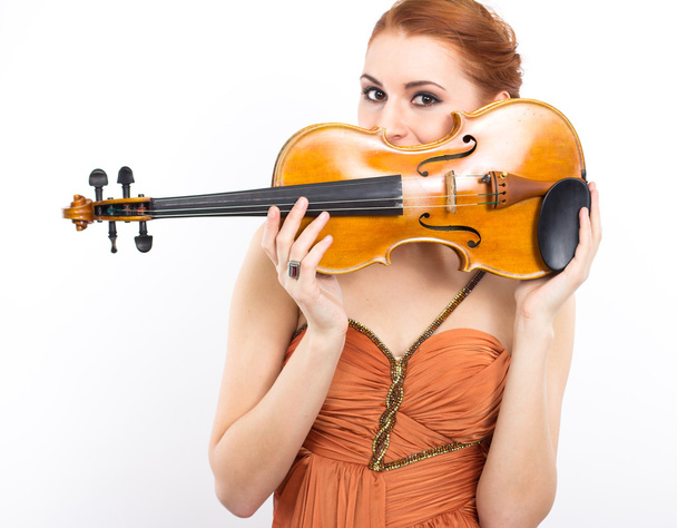Young red-haired girl with a violin in her hands on a white background.evening dress.Long orange dress - Photo, Image