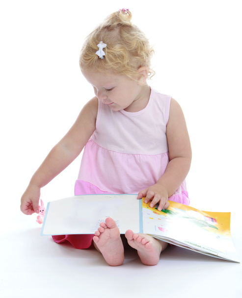 Adorable little girl sitting barefoot on the floor and reading a - Photo, image