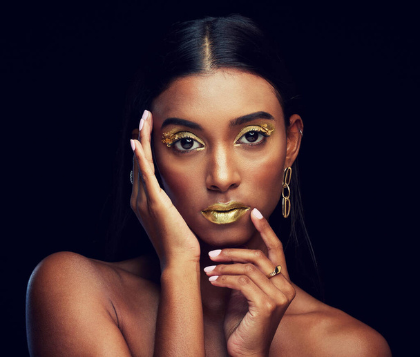 Gold makeup, serious and portrait of a woman isolated on a black background in a studio. Beauty, young and glamorous Indian model posing with creative cosmetics, jewelry and stylish on a backdrop. - Valokuva, kuva
