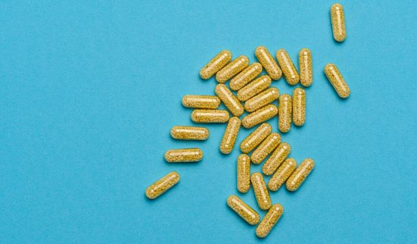 Transparente medizinische Kapseln mit gelbem Granulat innen auf blauem Hintergrund, Tabletten zur Behandlung, Vitamine - Foto, Bild