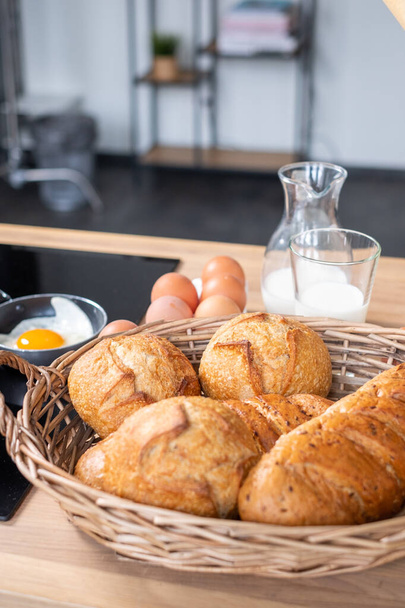 Φρέσκα καρβέλια ψωμί στο καλάθι στο τραπέζι. Λευκό γάλα σε  - Φωτογραφία, εικόνα
