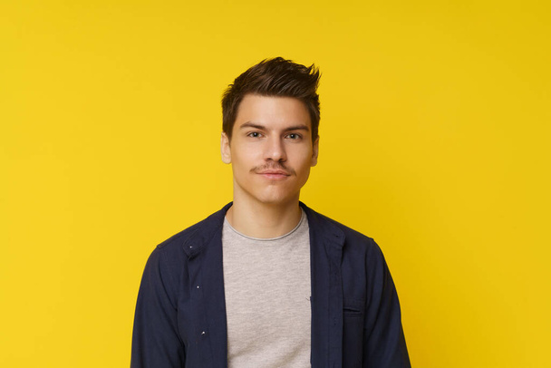 Serious and confident young man on yellow background. With neutral expression and looking directly at the camera, stylish and fashionable image portrays modern masculinity. High quality photo - Photo, image