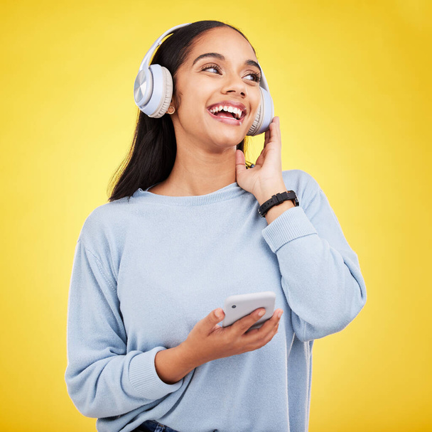 Happy, music and phone with woman in studio for streaming, online radio and audio. Smile, media and podcast with female and headphones on yellow background for technology, listening and connection. - Foto, immagini