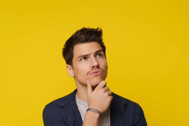 Close up of young man on yellow background, with facial expression conveying confusion and uncertainty, as he thinks and has doubt. Complex and emotional nature of decision-making and contemplation - Photo, Image