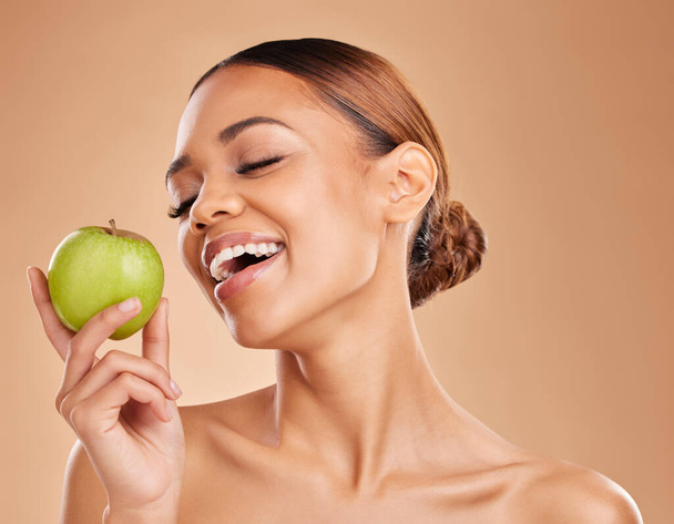 Beauty, skincare and woman with apple, healthy lifestyle and happiness against a brown studio background. Female, lady and fruit for diet, smile and cosmetics with treatment, smooth and soft skin. - Photo, image