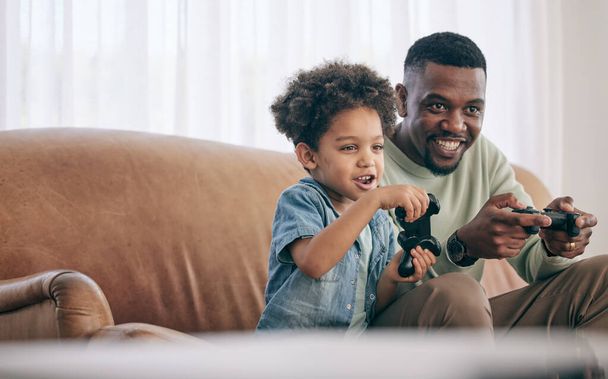 Black family, dad and child playing video games on living room sofa together with controllers at home. Happy African American father with son with smile enjoying bonding time on console entertainment. - Photo, Image
