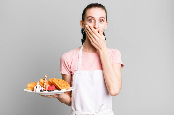 young pretty woman covering mouth with hands with a shocked. waffles concept - Foto, Imagen