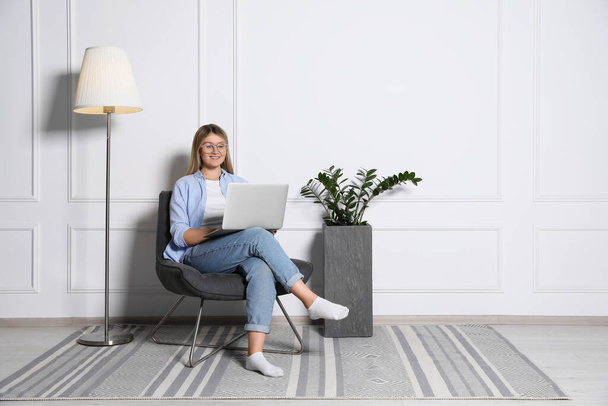 Jonge vrouw met laptop in de fauteuil thuis, ruimte voor tekst. Interieur ontwerp - Foto, afbeelding