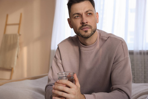 Upset man with glass of water in bedroom. Loneliness concept - Foto, immagini