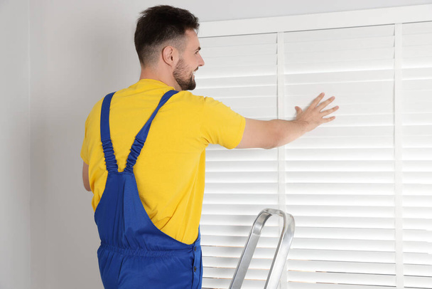 Worker in uniform installing horizontal window blinds indoors - Foto, imagen