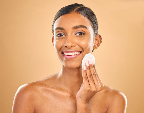 Skincare, happy and portrait of woman with cotton for facial cleansing isolated on a background. Smile, beauty and an Indian model cleaning her face with a pad for gentle treatment and makeup removal. - Foto, Bild