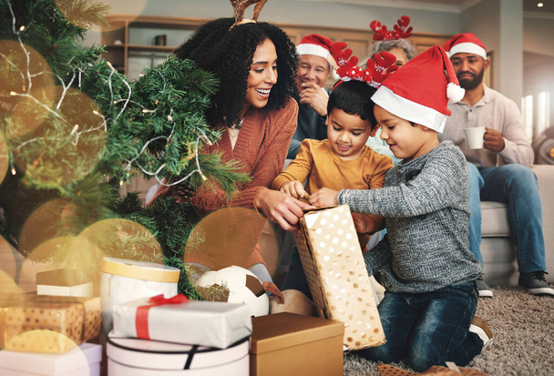 クリスマス、家族、男の子は贈り物を開き、休日を祝い、箱に満足しています。笑顔で、一緒にお祝いの季節に母親からプレゼントを開始し、興奮している子供たち. - 写真・画像