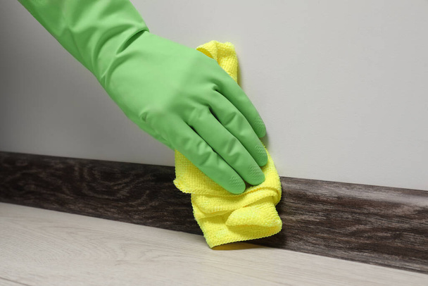 Женщина в перчатках, чистит плинтус с тканью в помещении, крупным планом - Фото, изображение