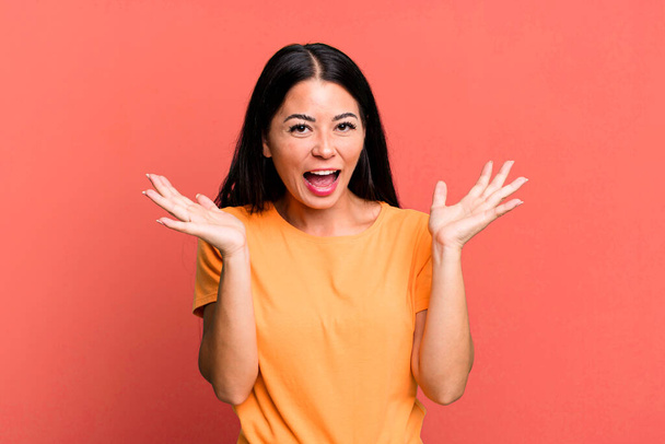 pretty latin woman looking happy and excited, shocked with an unexpected surprise with both hands open next to face - Foto, immagini