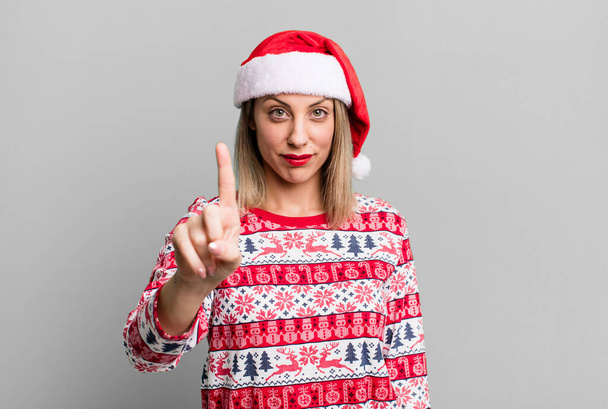 pretty blonde woman smiling and looking friendly, showing number one. christmas and santa hat concept - Фото, зображення