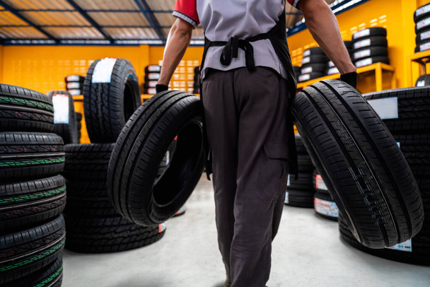 A male auto mechanic holding two tires in tire shop to change car wheels at service center or auto repair shop for auto industry. Automobile industry. - Foto, imagen