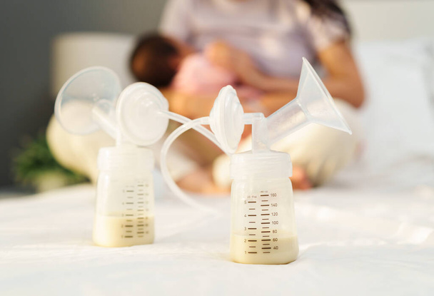 the breast milk are in the bottles of electric breast pumping set on a bed with mother breastfeeding newborm baby background - Foto, immagini