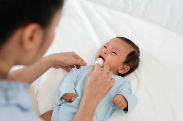 mother using finger to clean newborn baby mouth (tongue and gum) with clean gauze on a bed - Photo, image