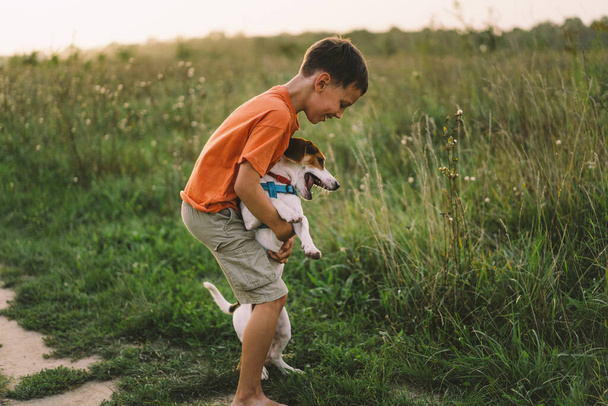 Portré egy kisfiúról, aki a Jack Russell kutyájával játszik a parkban. Fogalom az állatokról, barátságról, emberekről és szerelemről. Egy fiú egy Jack Russell terrierrel játszik. - Fotó, kép