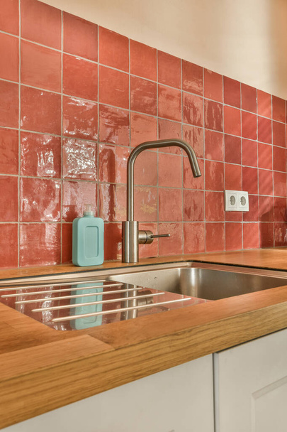 a kitchen with red tiles on the wall and wooden counter tops in front of the sink, which is being used for cleaning - Foto, Bild