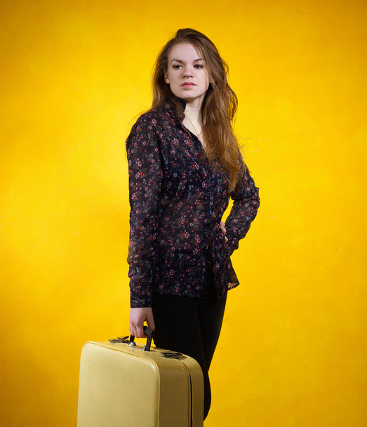girl with a suitcase on background of yellow wall - Valokuva, kuva