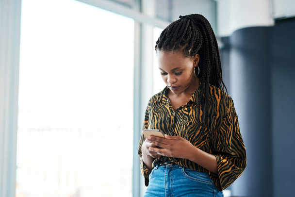 Ohne Vernetzung kann man nicht erfolgreich sein. eine attraktive junge Geschäftsfrau, die allein in ihrem Büro steht und auf ihrem Handy SMS schreibt - Foto, Bild