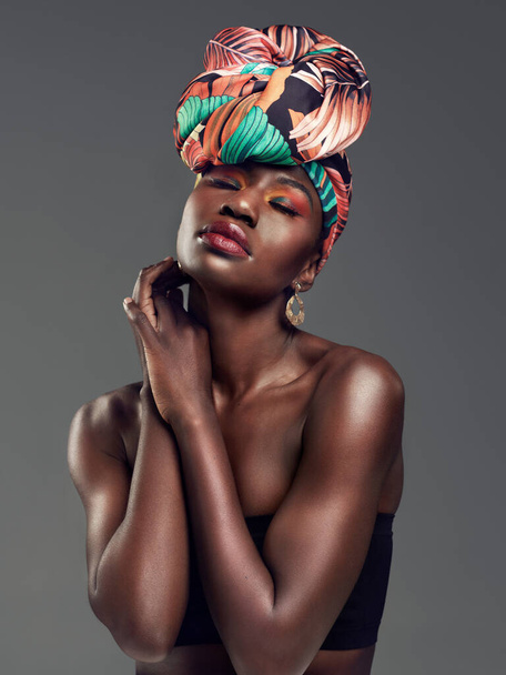 The undeniable beauty of a head wrap. Studio shot of a beautiful young woman wearing a traditional African head wrap against a grey background - Foto, Imagen