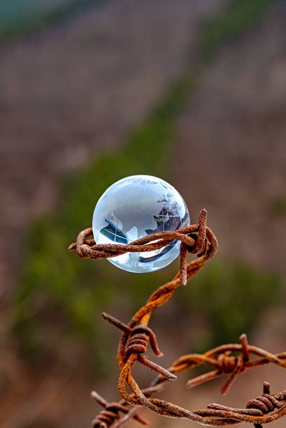 Het concept van symboliek. Op een herfst bos achtergrond is een glazen bol, die is omgeven door roestig prikkeldraad - Foto, afbeelding