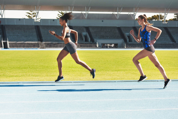 Ő szabja meg az iramot. Teljes hossz felvétel két vonzó fiatal női sportolóról, akik a pályán futnak. - Fotó, kép